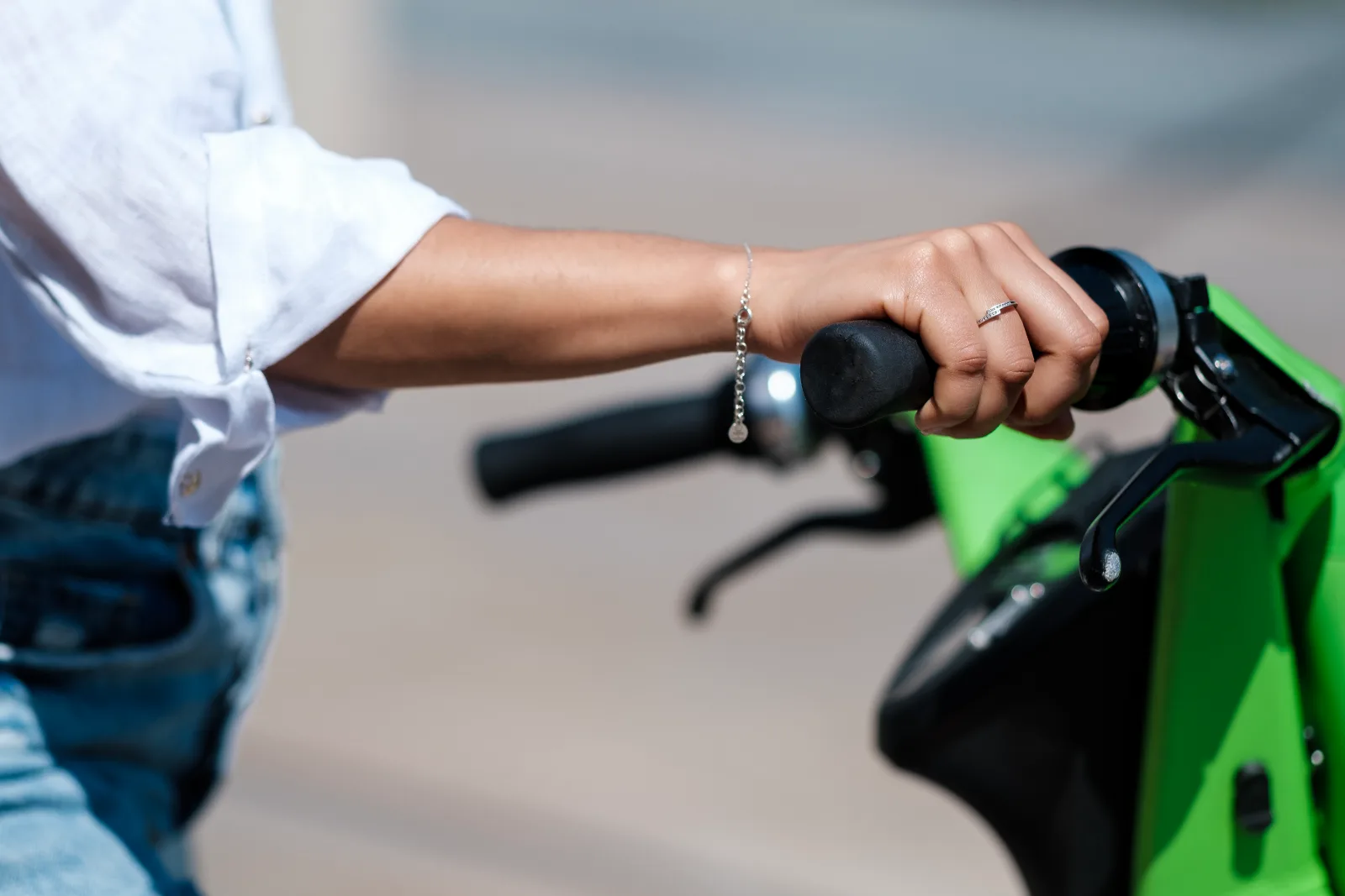 Hånd på styret af grøn elcykel med bremsegreb og ring på fingeren